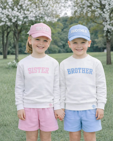 Two children wearing coordinating sweatshirts and hats with 'Sister' and 'Brother' 