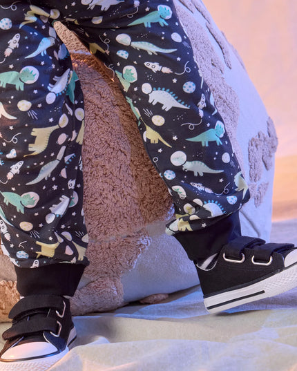 Close up of a boy wearing black pants covered in a colorful dinosaur space print.