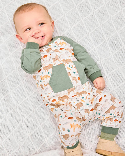 Baby wearing romper with green raglan sleeves, pockets, and cuffs, featuring an all-over woodland animal print.