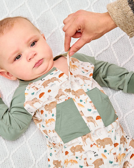 Baby wearing romper with green raglan sleeves, pockets, and cuffs, featuring an all-over woodland animal print.