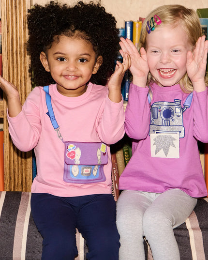 Two children sitting on a couch wearing pink and purple shirts 