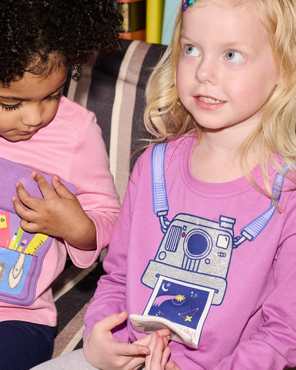 Two children sitting on a couch wearing pink and purple shirts 