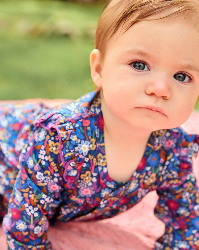 A baby wearing a long-sleeve floral romper crawls on a pink blanket outdoors