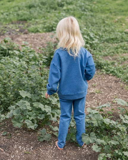 A young blonde girl wearing a matching blue sweatshirt and sweatpants set. 