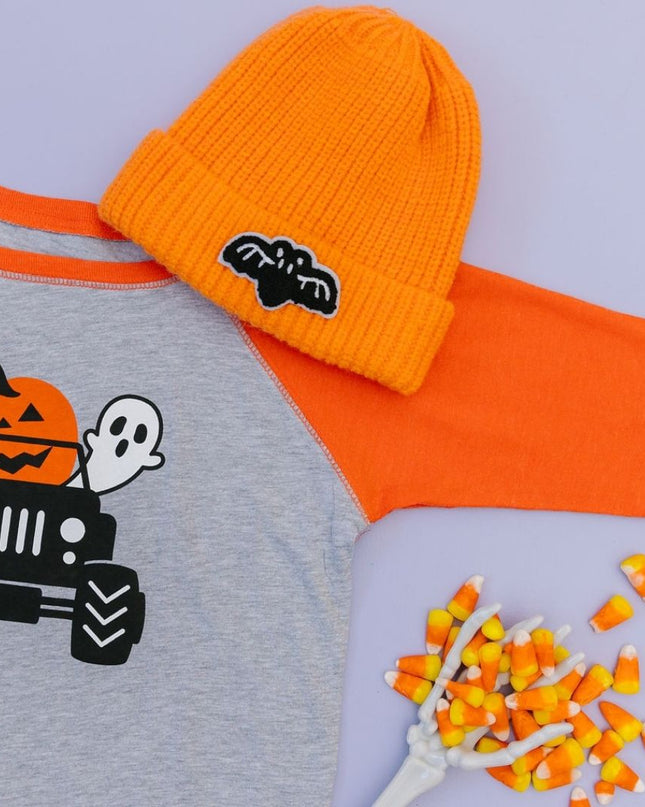 Flat lay showing T-shirt with truck, pumpkin, ghost and bat graphic, orange hat with bat patch and candy corn