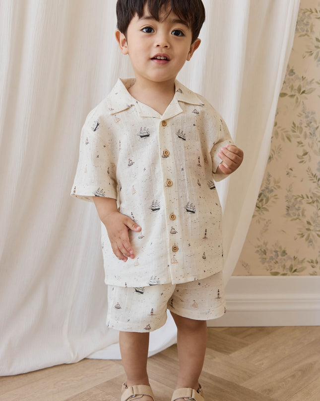 Boy wearing cream colored shirt and pants with sailboat print