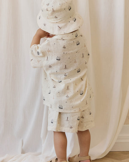 Boy wearing cream colored shirt and pants with sailboat print