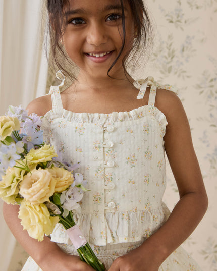 Girl wearing cream and floral top holding yellow flowers