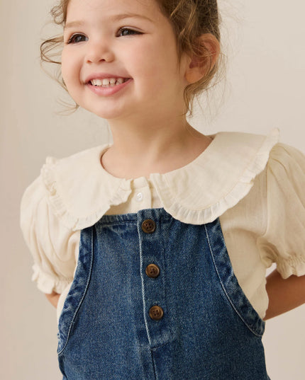 Girl wearing white blouse with blue denim overalls