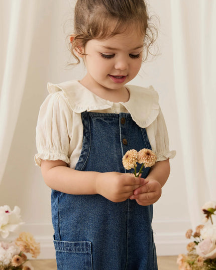 Girl wearing white blouse with blue denim overalls