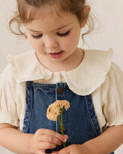 Girl wearing white blouse with blue denim overalls