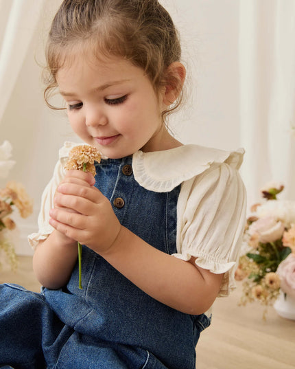 Girl wearing white blouse with blue denim overalls
