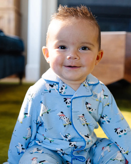 A smiling baby wearing light blue long-sleeve pajama coveralls with a cartoon dog pattern on roller skates.