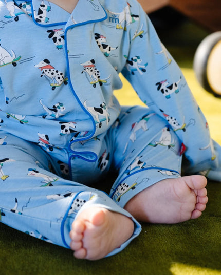 A baby wearing light blue long-sleeve pajama coveralls with a cartoon dog pattern on roller skates.