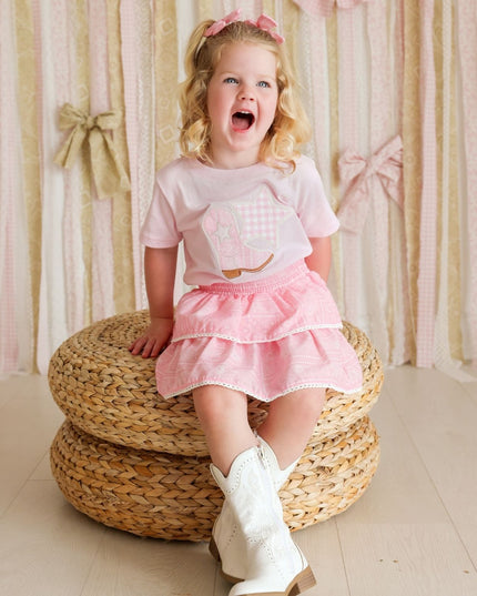 Girl wearing pink t-shirt with cowboy boot and star patch and bandana skirt