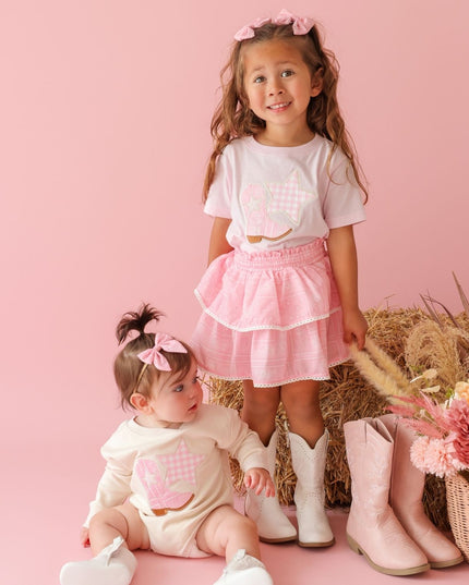 Girl wearing pink t-shirt with cowboy boot and star patch and bandana skirt and baby wearing romper with cowboy boot and star