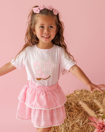 Girl wearing pink t-shirt with cowboy boot and star patch and bandana skirt