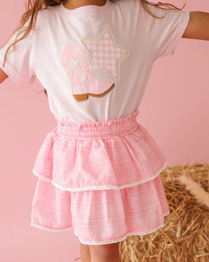 Girl wearing pink t-shirt with cowboy boot and star patch and bandana skirt