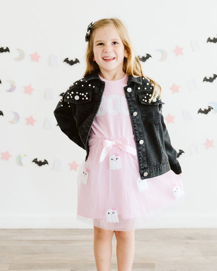 A girl wearing a pink tutu dress with sequin 'Boo' and ghost details and a black denim jacket with pearls