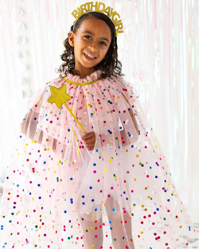 Girl wearing pink polka dot cape with gold birthday girl headband and holding a gold star wand