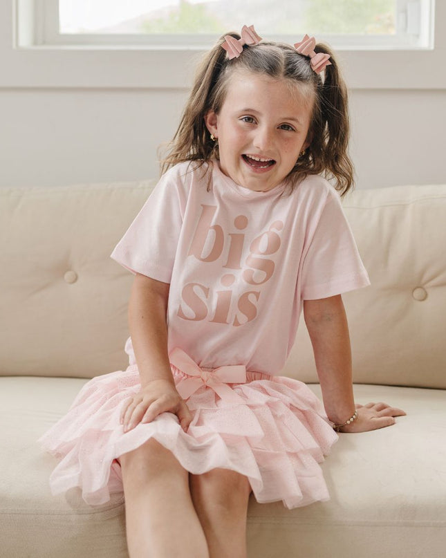 Girl wearing a pink 'big sis' outfit sitting on a couch.