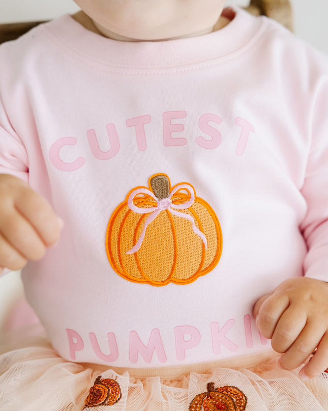 Baby wearing a long sleeve pink baby romper with pumpkin patch and text 'cutest pumpkin'