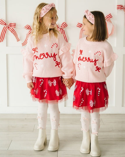 Girls wearing red tutus with red and white sequin candy canes and bows and pink merry sweaters