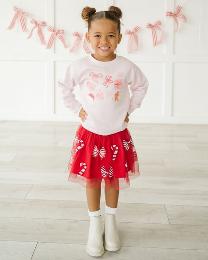 Girl wearing pink crewneck sweatshirt with fun Christmas graphics and red tutu with candy canes and bows