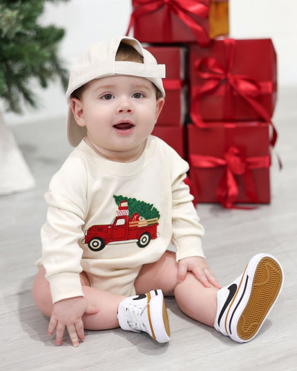 Baby wearing natural color long sleeve romper with a red tuck carrying a Christmas tree patch