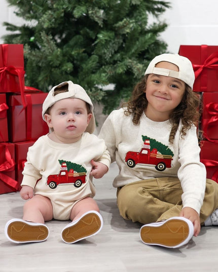 Boy and baby wearing complimentary sweatshirts and rompers with red truck carrying Christmas trees