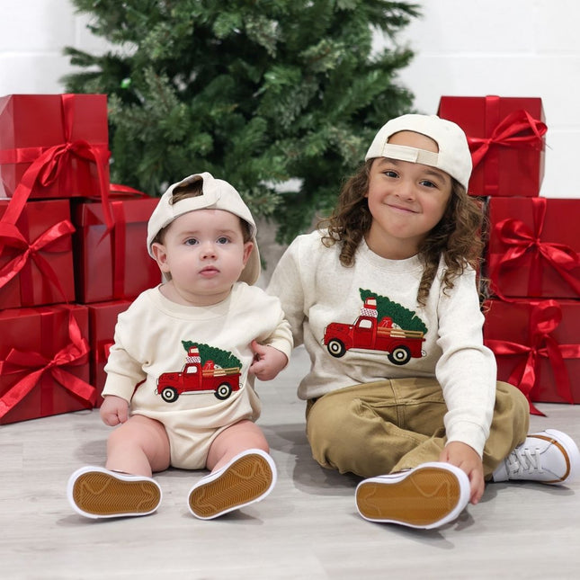 Boy and baby wearing complimentary sweatshirts and rompers with red truck carrying Christmas trees