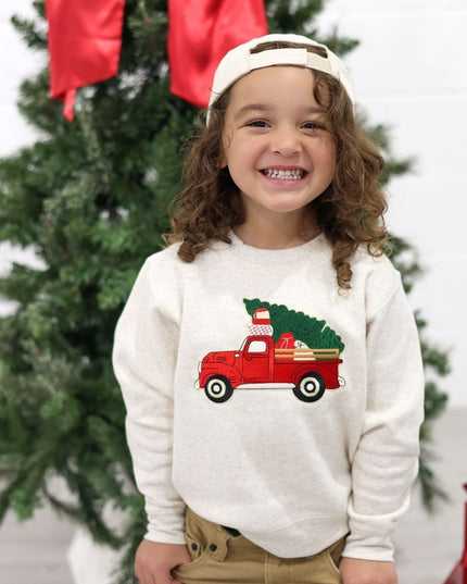 Boy wearing a natural color sweatshirt with red truck carrying a Christmas tree patch and hat with a Christmas tree