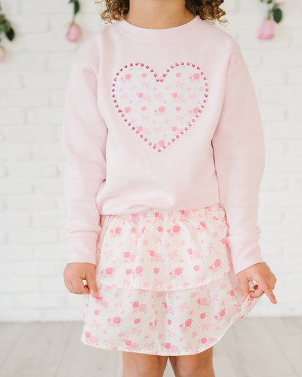 Girl wearing pink sweatshirt with floral and pearl heart patch and skirt