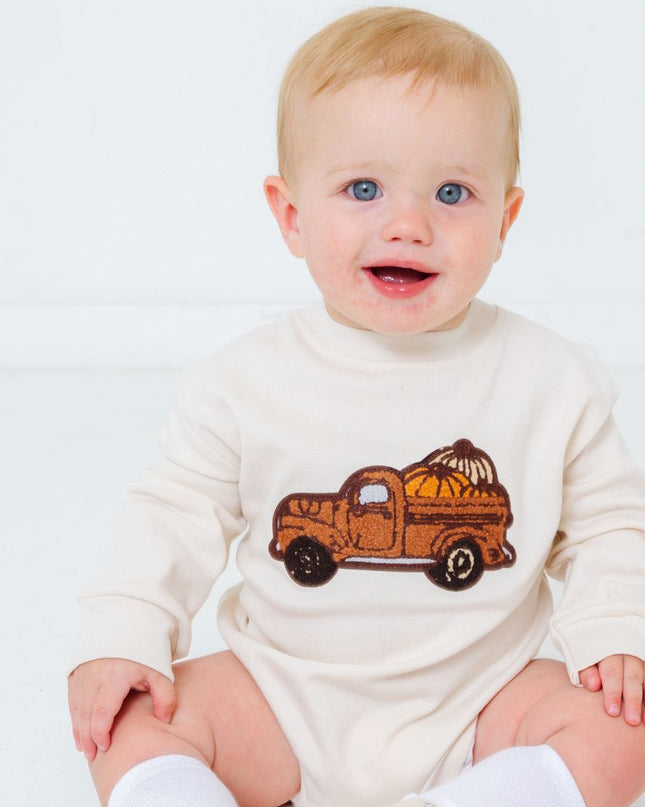 Baby wearing romper with truck carrying pumpkins