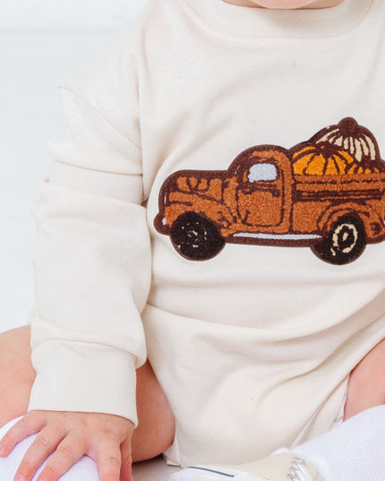 Baby wearing romper with truck carrying pumpkins