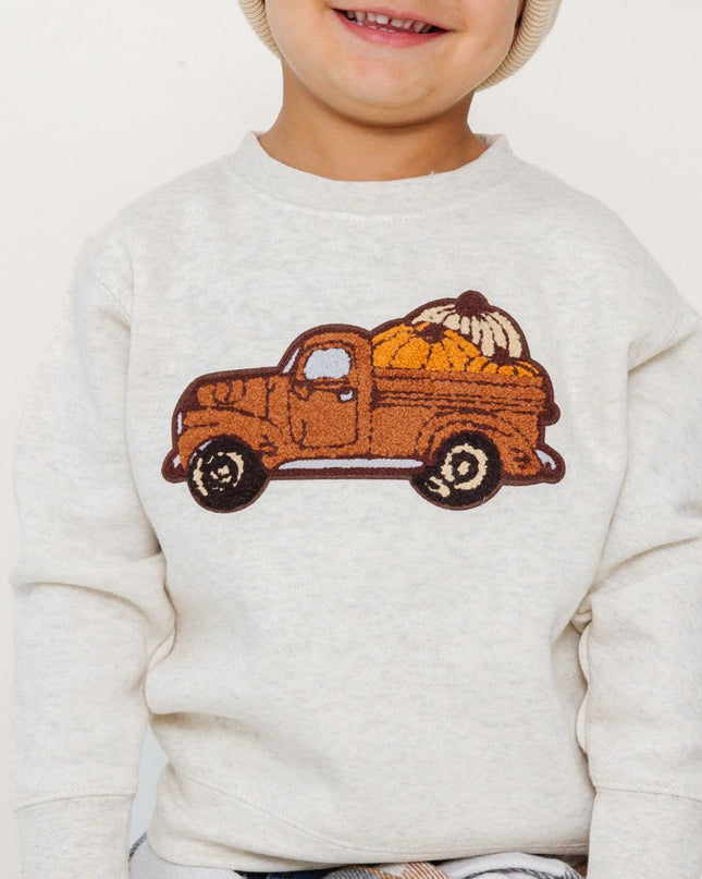 Boy wearing sweatshirt with truck carrying pumpkins