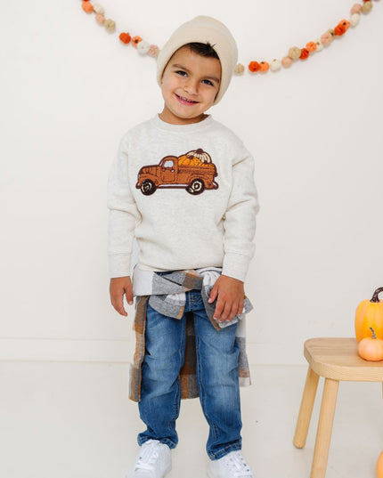 Boy wearing sweatshirt with truck carrying pumpkins