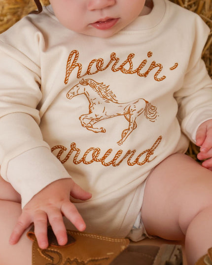 Baby wearing romper with 'horsin' around' graphic