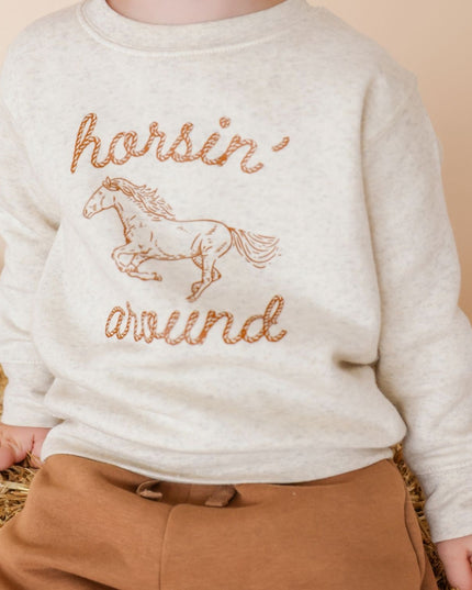 Boy wearing sweatshirt with 'horsin' around' graphic and brown pants