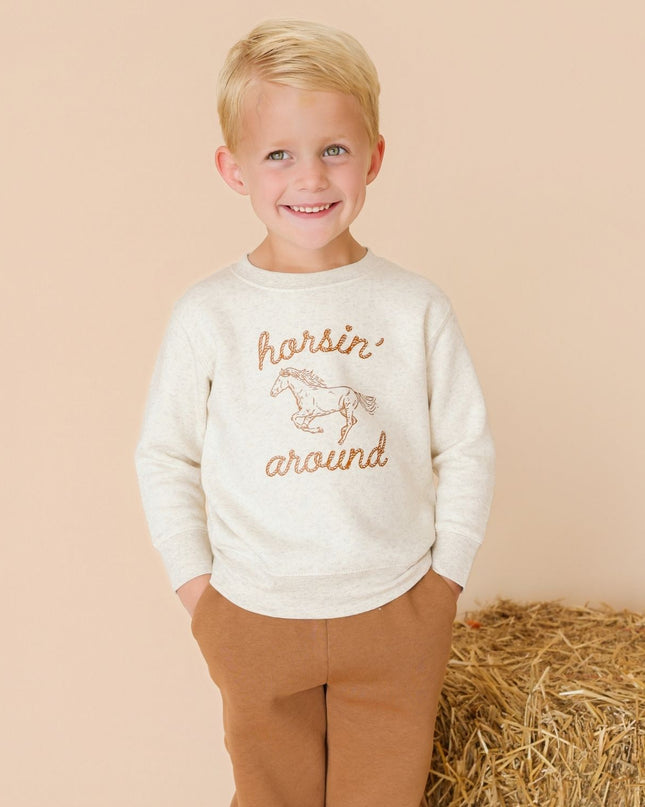 Boy wearing sweatshirt with 'horsin' around' graphic and brown pants