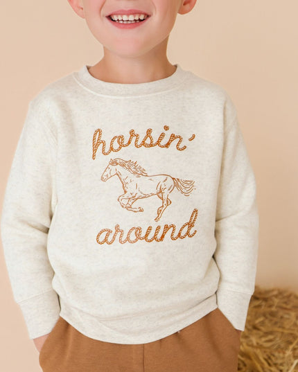 Boy wearing sweatshirt with 'horsin' around' graphic and brown pants