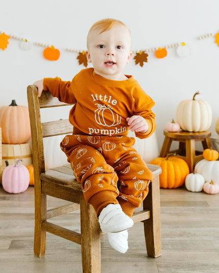 Baby wearing orange baby romper with 'little pumpkin' graphic and pumpkin sweatpants