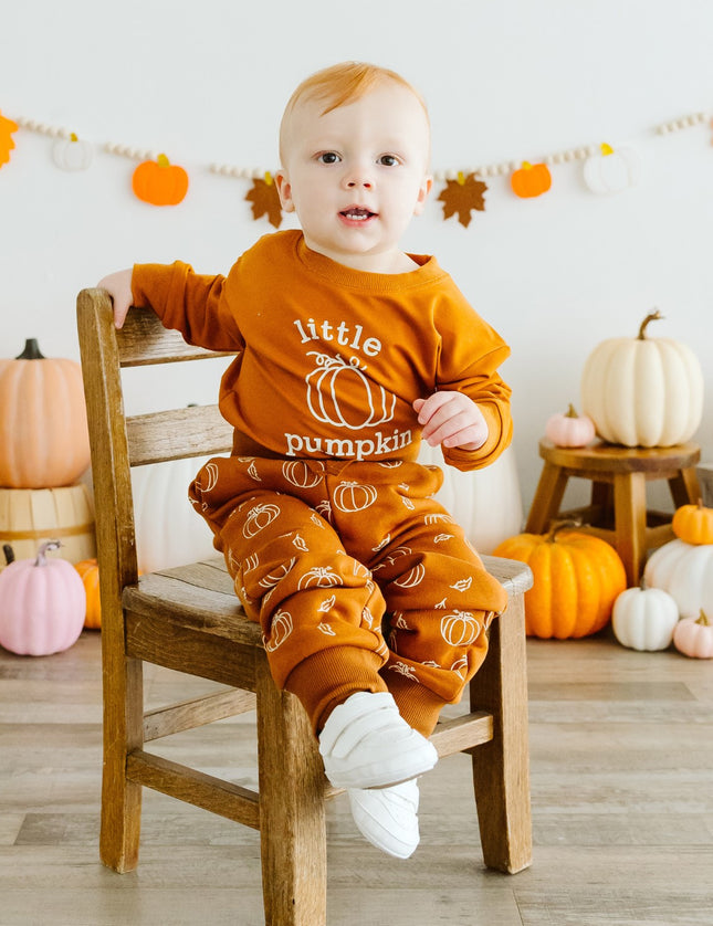 Baby wearing orange baby romper with 'little pumpkin' graphic and pumpkin sweatpants