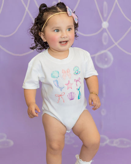 Baby wearing white romper with mermaid graphics