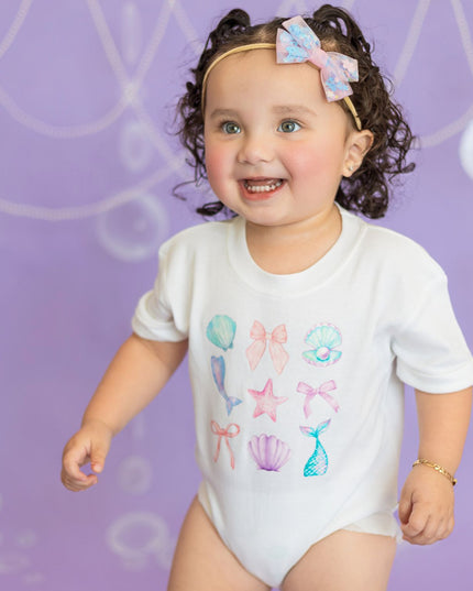 Baby wearing white romper with mermaid graphics