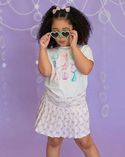 Girl wearing white mermaid graphic t-shirt and purple bow skort