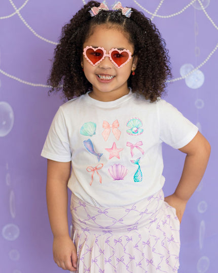 Girl wearing white mermaid graphic t-shirt and purple bow skort