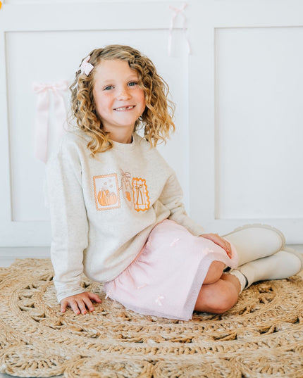 Young girl sitting wearing a pink tutu and pumpkin sweatshirt