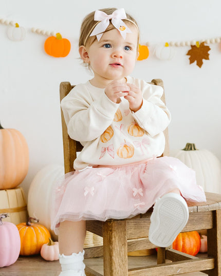 Baby sitting on a chair wearing a pink tutu and pumpkin sweatshirt