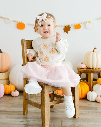 Baby sitting on a chair wearing a pink tutu and pumpkin sweatshirt